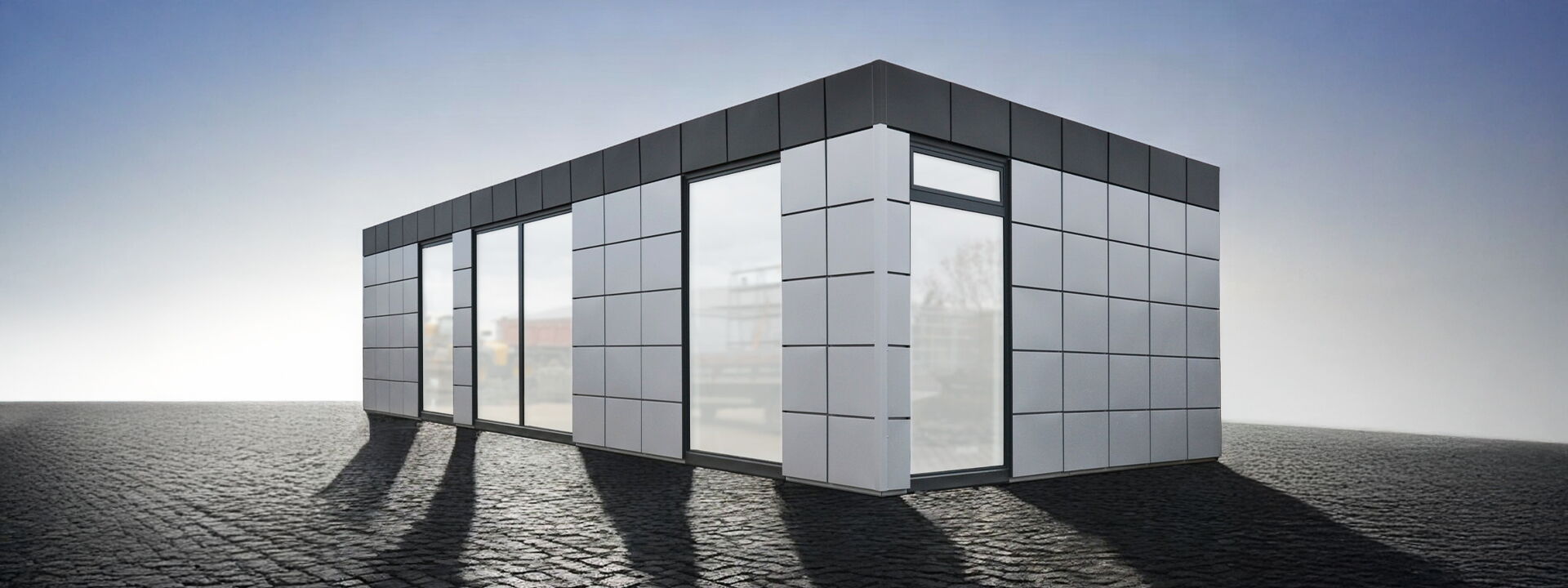Conteneur de bureau moderne avec façade à trame grise et grandes fenêtres toute hauteur sur une surface pavée      