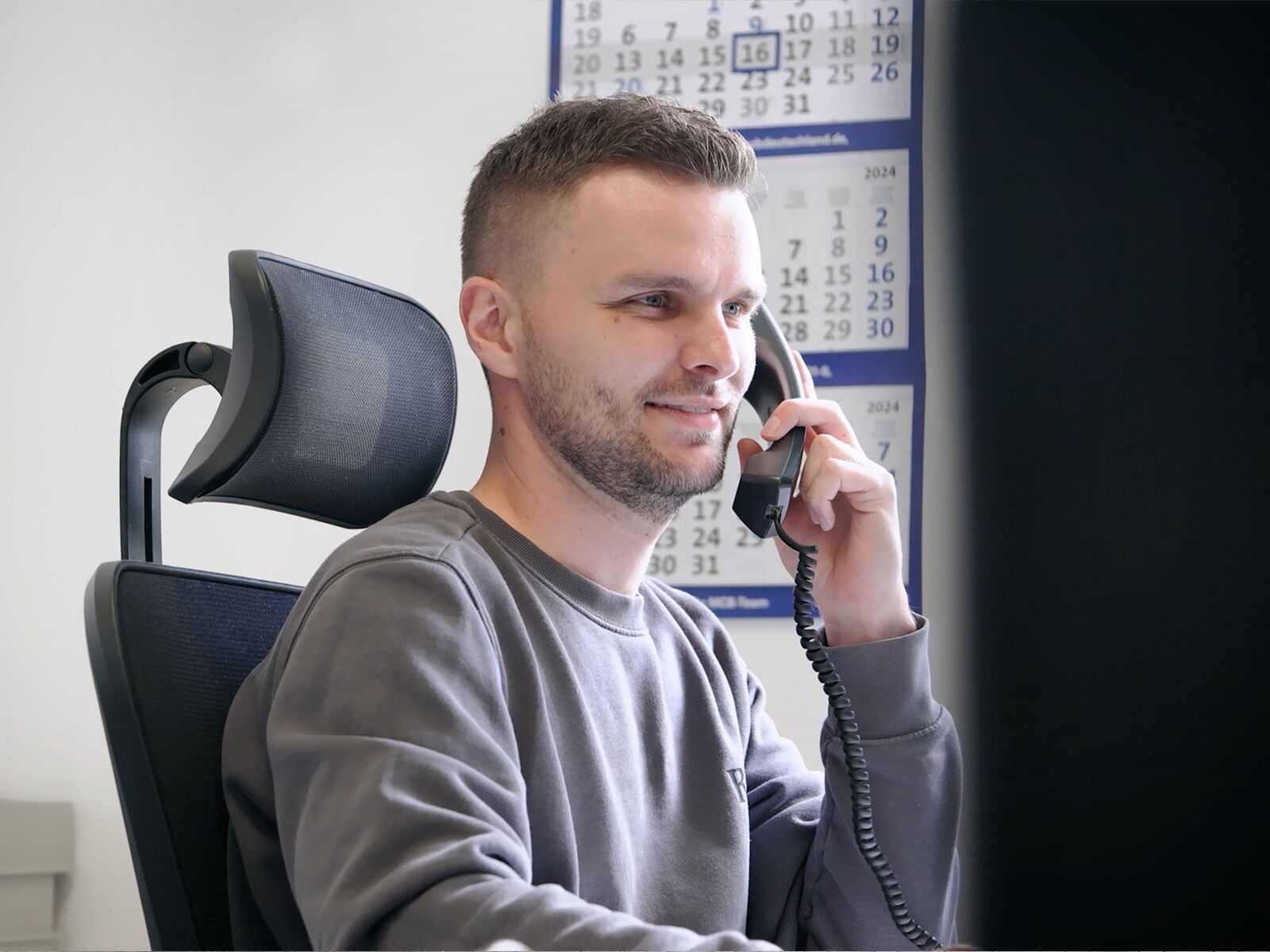 Employé au bureau assis à son bureau en train de téléphoner avec un téléphone fixe      